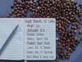Health benefits of coffee - words handwritten in a notepad. Spilled coffee beans in the background, healthy diet concept