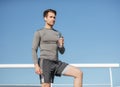 Health and body care. Muscular handsome guy in sportswear, with wireless headphones holding bottle of water on blue sky