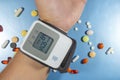 Health care. Closeup of wrist blood pressure monitor with colorful pills on blue background for medical design.