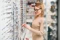 Health care, eyesight and vision concept - happy woman choosing glasses at optics store. Portrait of beautiful young Royalty Free Stock Photo