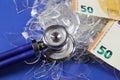 Health care system collapse concept: euro money bill notes on pile of broken glass shards, stethoscope, blue background focus on Royalty Free Stock Photo