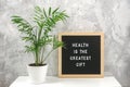 Health is the greatest gift. Motivational quote on letter board on white table and green exotic palm flower in pot, gray stone Royalty Free Stock Photo