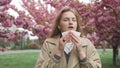 Pretty young Caucasian woman having alergy symptoms from blooming sakura tree pollen in spring. Female with pollen