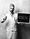 Health professional with beard and confident face expression holds blackboard with word medicine on it and shows thumbs