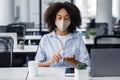 Health protection and new normal in workplace. African american young woman in protective mask disinfects hands with