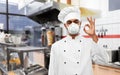 Chef in respirator showing ok sign at kitchen