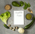 Diet plan with greens and fresh vegetables in a paper notebook with with words Helth tips on a gray table surface.