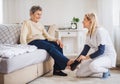 A health visitor putting on slippers on a senior woman at home at Christmas time. Royalty Free Stock Photo