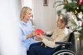 Health visitor and senior woman in wheelchair with a present at home at Christmas. Royalty Free Stock Photo