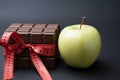 Health vs indulgence Apple, ribbon, chocolate on contrasting background