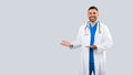 Healthcare ad. Positive male physician pointing aside at free space with two hands, panorama with free place for design