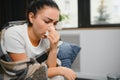 healthcare, cold, allergy and people concept - sick woman blowing her runny nose in paper tissue at home.