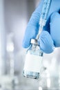 Health care concept with a hand in blue medical gloves holding a vaccine vial with blue liquid and black white label Royalty Free Stock Photo