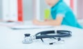 Little boy writes on clipboard sitting at doctor`s desk. Stethoscope in the foreground. Focus on the stethoscope.