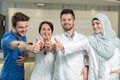 Healthcare and medicine concept - attractive male doctor in front of medical group in hospital showing thumbs up