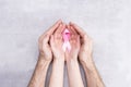 Healthcare and medicine concept - female and male hands hold pink breast cancer awareness ribbon on gray background