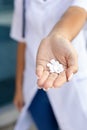 Oriental female hands of a pharmacist in a medical gown holding a handful of white pills in the palm outside