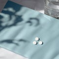 Healthcare minimal lifestyle concept. White pills on blue notebook with aesthetic sunlight shadows