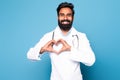Healthcare professional. Happy indian male doctor showing heart gesture with hands posing on blue background Royalty Free Stock Photo