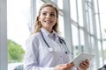 Healthcare, technology and medicine concept - smiling female doctor with stethoscope taking notes at tablet pc computer. Royalty Free Stock Photo