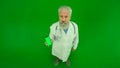 Portrait of man medic in studio on chroma key green screen. Senior doctor in white uniform looking at camera and holding Royalty Free Stock Photo