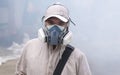 Healthcare worker in multi-purpose respirator half mask with protective clothing looking at camera on chemical fume background