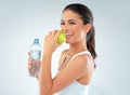 Healthiness is happiness. Studio shot of a fit young woman holding a bottle of water and an apple against a gray Royalty Free Stock Photo