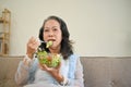 Healthy Asian aged woman eating salad while watching TV in her living room Royalty Free Stock Photo