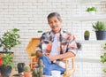 Healthy Asian senior man with mustache sitting  at table indoor with houseplants and gardening tool , smiling and looking at Royalty Free Stock Photo