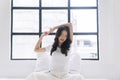 Healthy asian woman waking up relax muscles beside window early in morning. Happy young girl stretching raised arms muscles body Royalty Free Stock Photo