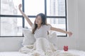 Healthy asian woman waking up relax muscles beside window early morning. Happy young girl stretching raised arms muscles body cozy Royalty Free Stock Photo