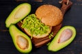 Healthy avocado burger on the wooden board - traditional Mexican dish. Vegetarian avocado sandwich on the black kitchen background Royalty Free Stock Photo