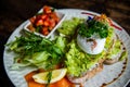 Healthy avocado toast on gluten free bread with poached eggs and green salads with tomatos on white plate in cafe. Royalty Free Stock Photo