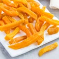 Healthy baked sweet potato fries on white plate served with spicy sauce, square