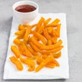 Healthy baked sweet potato fries on white plate served with spicy sauce, square format