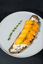 Healthy balanced food sandwich with persimmon and soft cheese on black background.