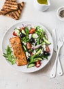 Healthy balanced lunch - grilled red fish fillet salmon and tomatoes, cucumbers, olives, feta Greek salad on a light background, Royalty Free Stock Photo
