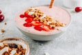Healthy banana and strawberrie smoothie in a bowl with pieces of strawberries, granola and coconut chips
