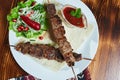 Healthy barbecued lean cubed pork kebabs served with a corn tortilla and fresh lettuce and tomato salad, close up view