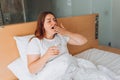 Healthy beautiful young girl holding glass of water on bed at home. Woman waking up in the morning yawning. Concept of Royalty Free Stock Photo