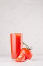 Healthy beverage - fresh vegetable tomato juice, straw, salt and red tomatoes on soft white wood background, copy space, vertical. Royalty Free Stock Photo