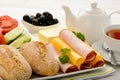 Healthy breakfast with cheese, ham, fresh bun, fresh vegetables, olives and tea.