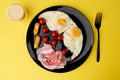 A healthy breakfast - coffee, scrambled eggs, bacon, cheese and cherry tomatoes. Food in a black plate on a yellow background. Royalty Free Stock Photo