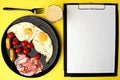 A healthy breakfast - coffee, scrambled eggs, bacon, cheese and cherry tomatoes. Food in a black plate on a yellow background. Royalty Free Stock Photo