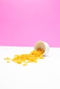 Healthy breakfast concept, Cornflakes poured out of container on pink white background