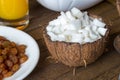 Healthy breakfast concept. Diced coconut meat in shell on wooden table with raisins on white plate.