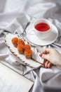 Healthy breakfast concept with a red caviar pancakes in female hand and cup of fruit tea in bed. Open book lie nearby. Royalty Free Stock Photo