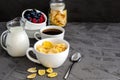 Healthy breakfast with cornflakes in a white cup, berries, milk and coffee on a dark gray background. Royalty Free Stock Photo