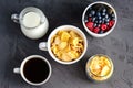 Healthy breakfast with cornflakes in a white cup, berries, milk and coffee on a dark gray background. Royalty Free Stock Photo