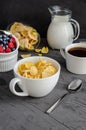 Healthy breakfast with cornflakes in a white cup, berries, milk and coffee on a dark gray background. Royalty Free Stock Photo